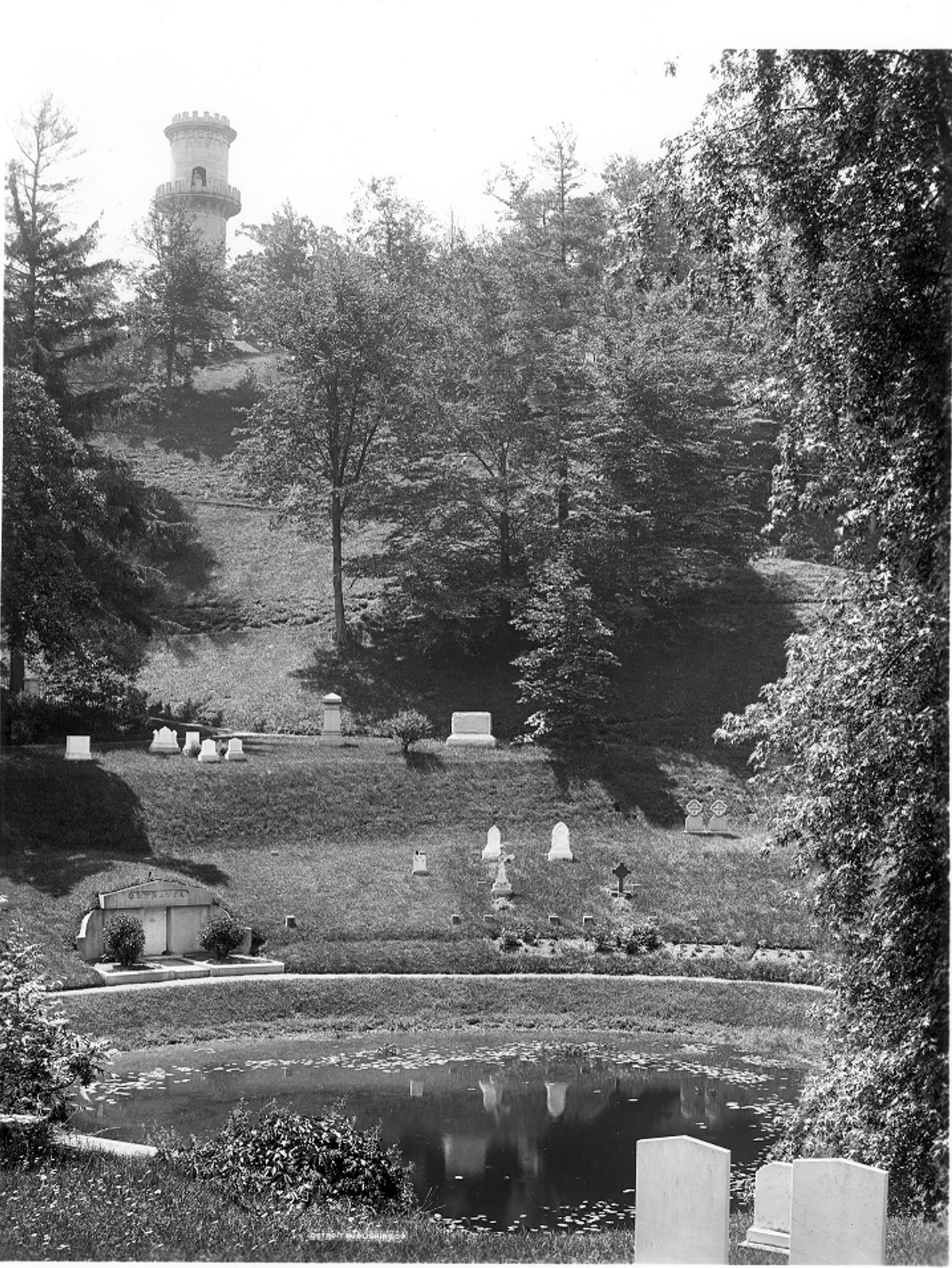 A black and white photograph of a cemetery with a view to a granite tower on the hill.